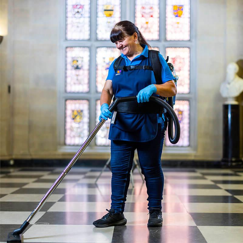 A Mitie female cleaning employee using a vacuum cleaner in front of stained glass windows